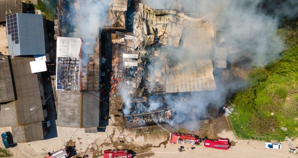 Aerial view of firefighters extinguishing ruined building on fire with collapsed roof and rising